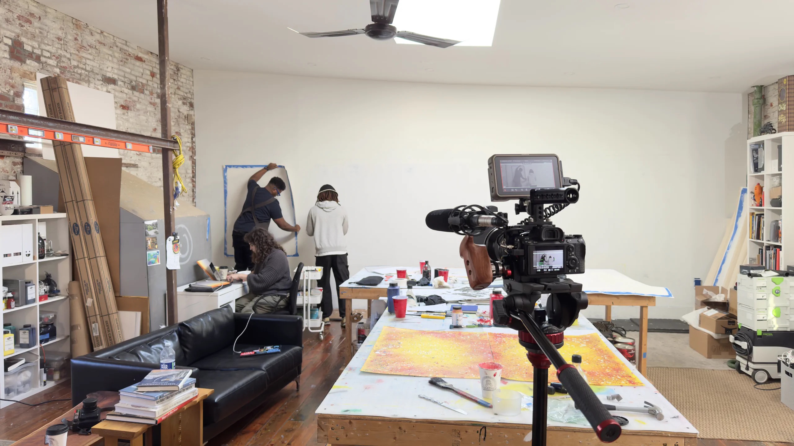 A cinema camera frames the crew working with Mark Thomas Gibson in his studio