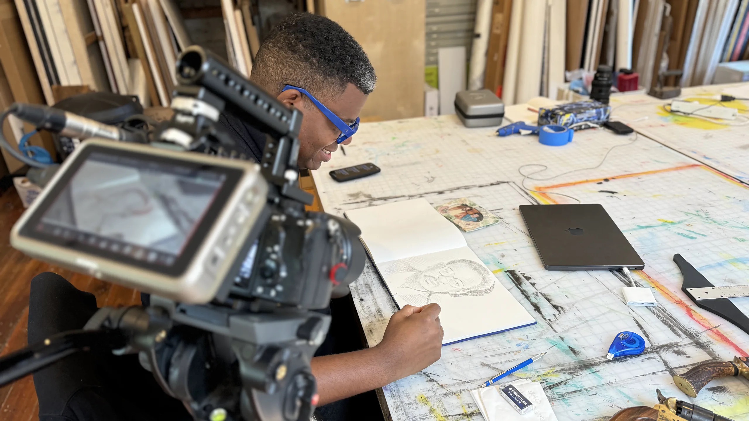Mark Thomas Gibson sketches at his worktable beside a cinema camera
